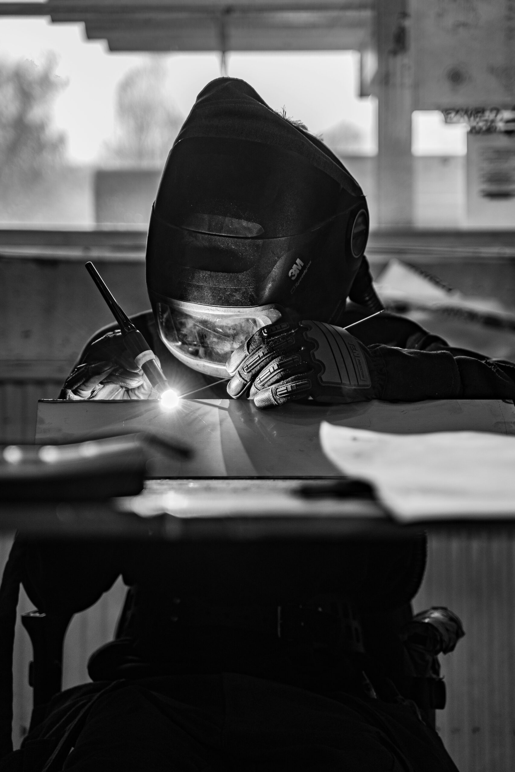 Operatore industriale impegnato in un’operazione di saldatura manuale, con maschera protettiva e guanti di sicurezza, durante una lavorazione metallica.
