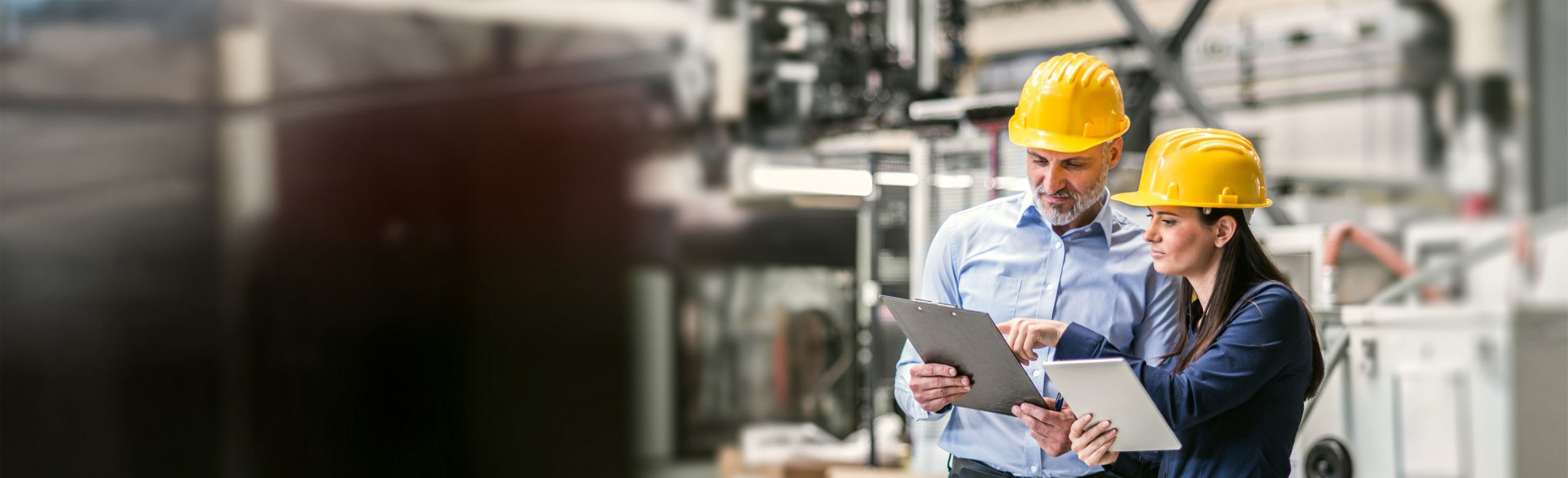 Due professionisti in ambito industriale, dotati di dispositivi di protezione individuale, consultano documentazione tecnica su tablet durante un controllo in fabbrica.