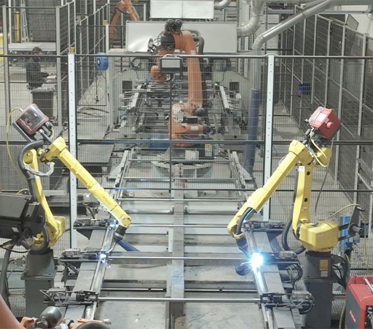 Automated production line with anthropomorphic industrial robots performing assembly and welding operations inside an industrial plant.