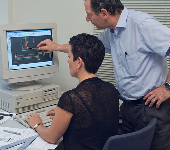 Archive image from the early years of Satech at the Calco site, showing two professionals analysing a technical drawing on a computer during a design activity.