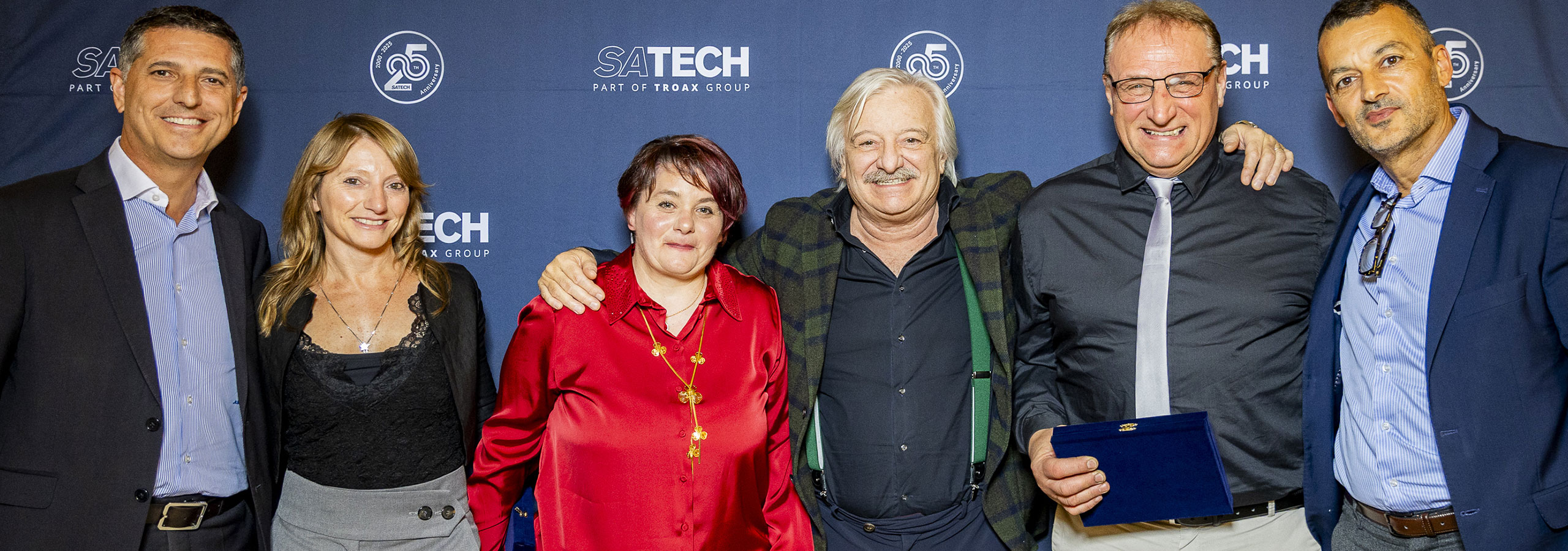 Gruppo di manager e dipendenti di Satech in posa davanti al backdrop brandizzato durante una cena aziendale.