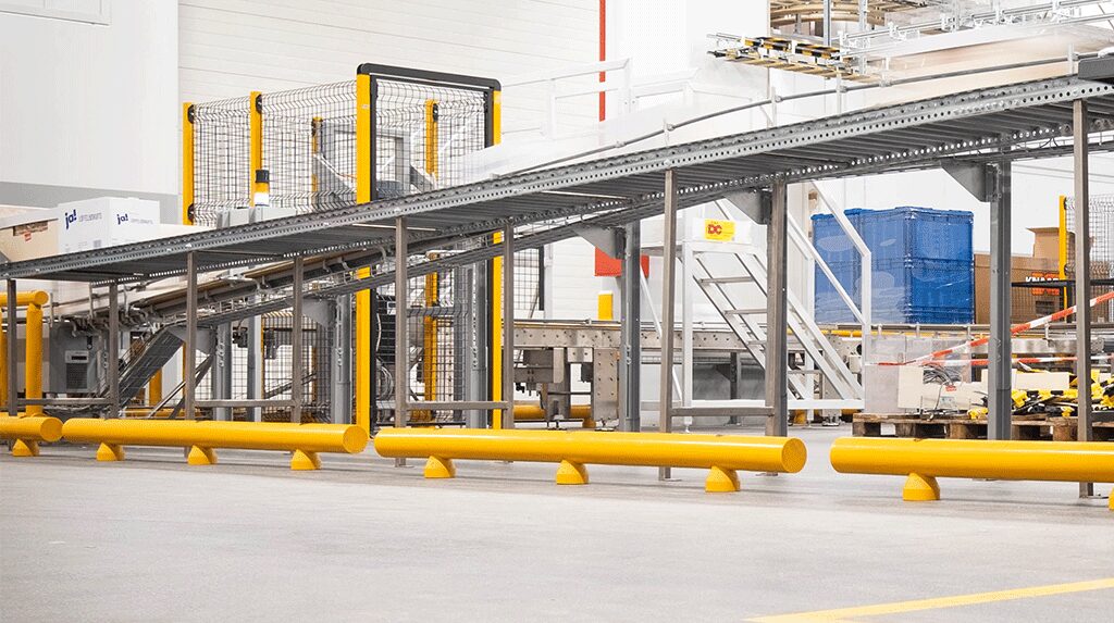 Nastro trasportatore sopraelevato con barriera di sicurezza gialla e recinzione metallica in magazzino logistico